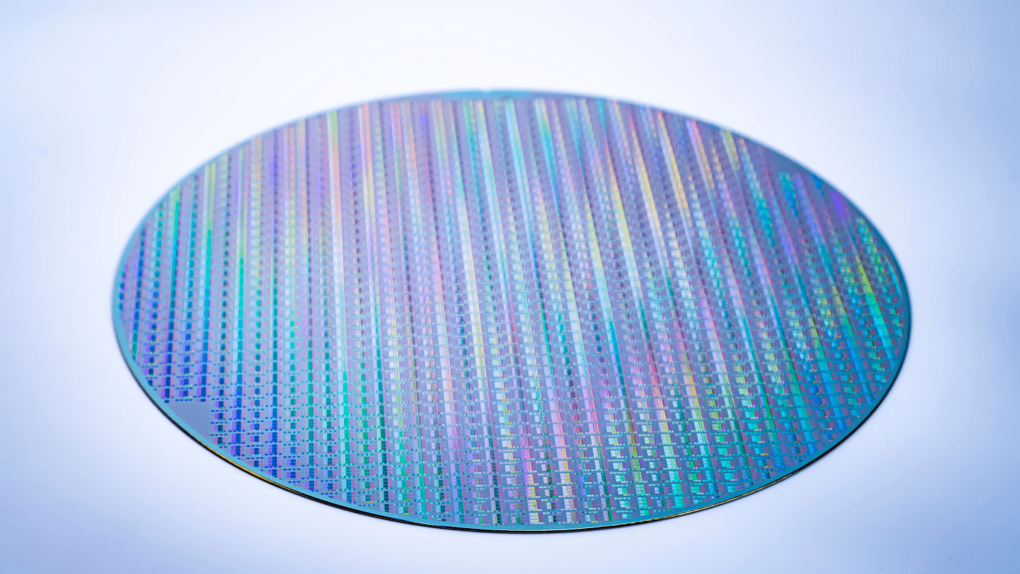 Close-up of a round silicon wafer with colorful, iridescent integrated circuit patterns etched across its surface.